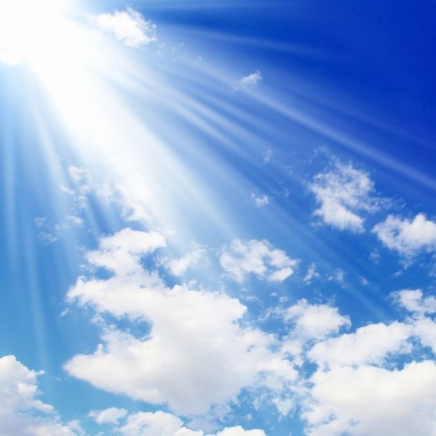 image of rays from the sun across the blue and lightly clouded sky.