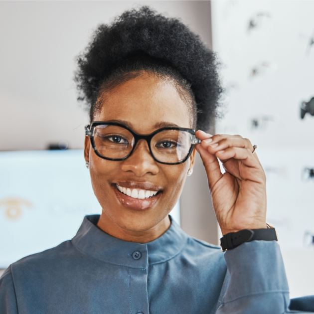 A smiling woman trying on glasses at an optical store.