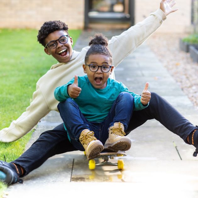 Kids wearing glasses playing on a skateboard.