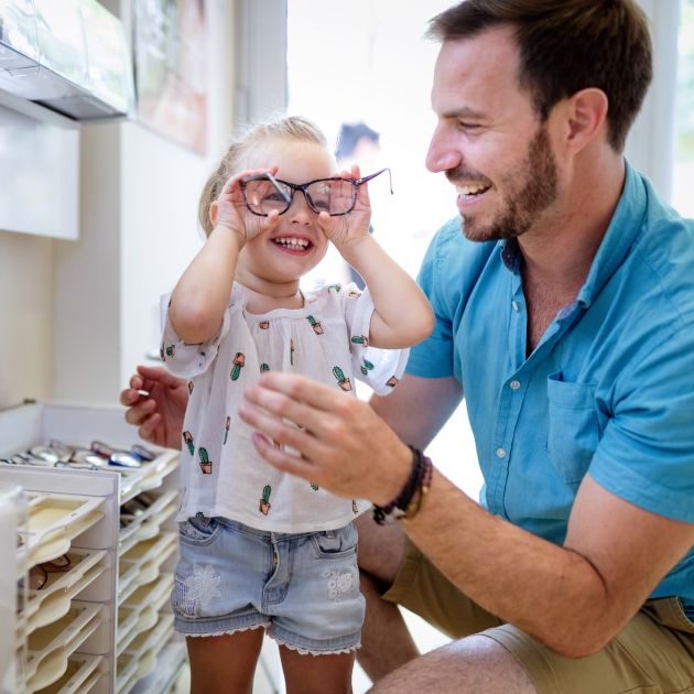 Toddler laughing and trying on glasses in store