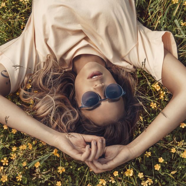 A woman lying down on grass with flowers, wearing MODO ECO eyewear.