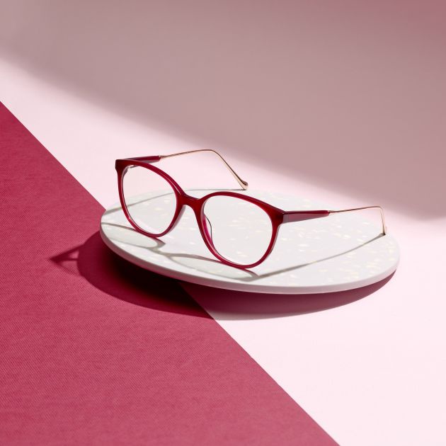 A red glasses frames on a pink background.