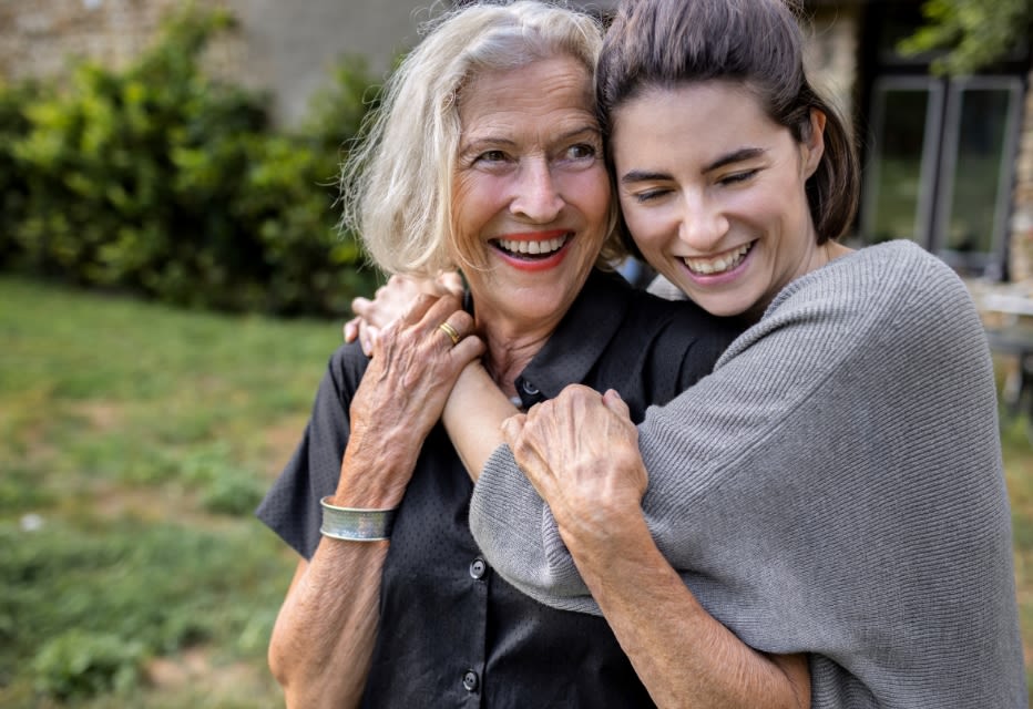 Two women (grandmother and granddaughter) hugging and smiling in a garden.