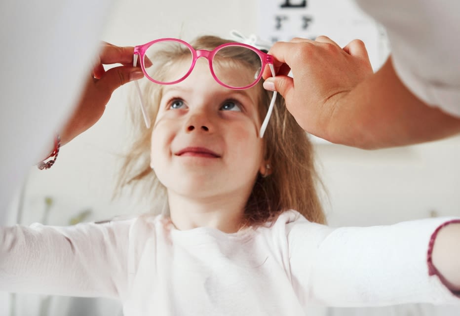 A woman adjusting glasses on a young girl.