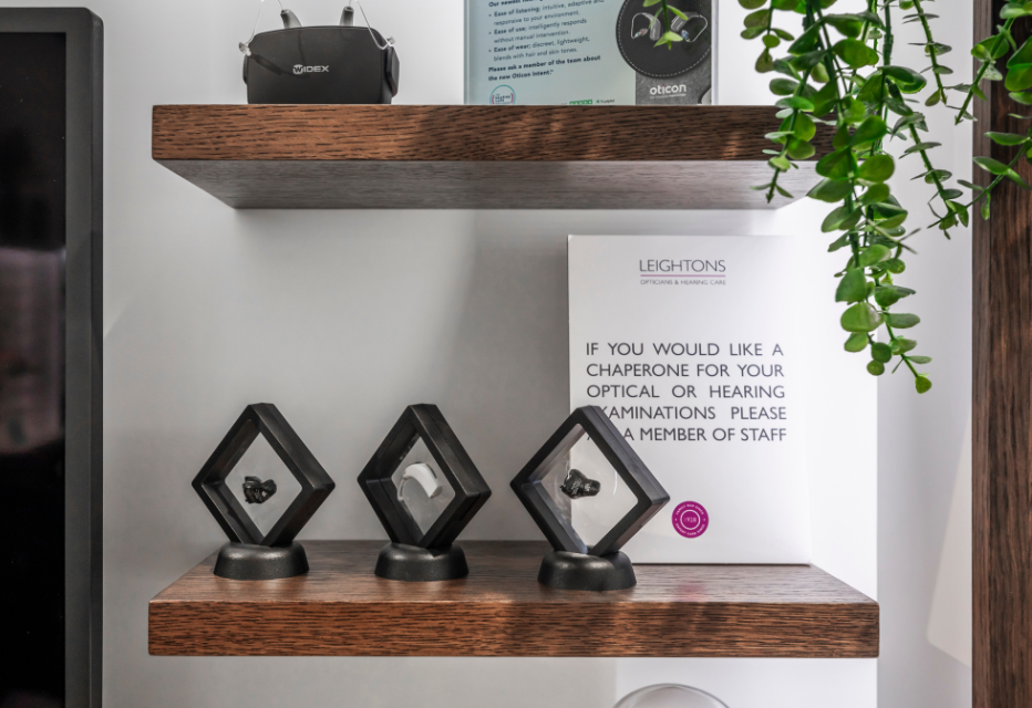 Three different styles of hearing aids displayed on a shelf at a Leightons branch, showcasing various designs.