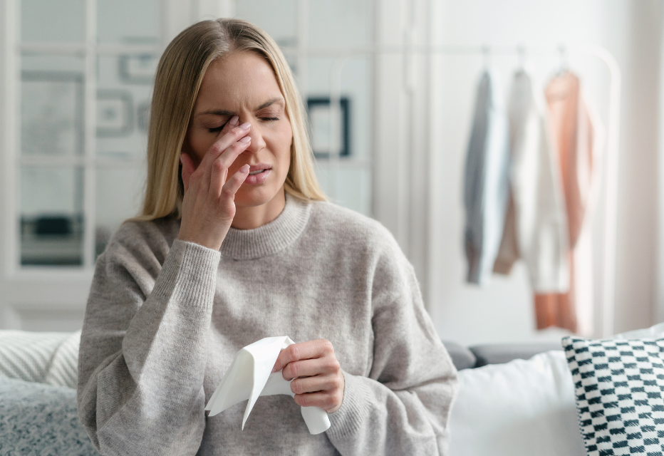 A woman appearing to be in pain while touching her eye, expressing discomfort or irritation.