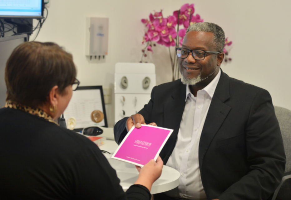 An audiologist handing a leaflet about hearing care packages to a patient, highlighting personalised support and options for hearing health.