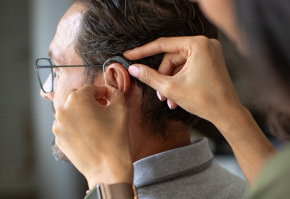 Close-up of a woman fitting a hearing aid on a man.
