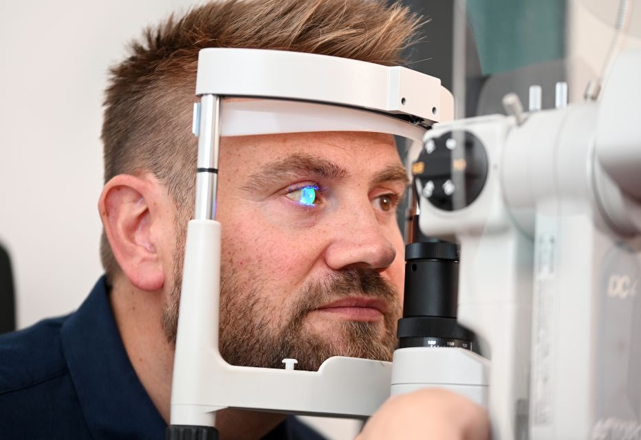 A patient undergoing an eye examination, seated at a slit lamp biomicroscope while an eye doctor uses the bright light to closely inspect the eye's structures.