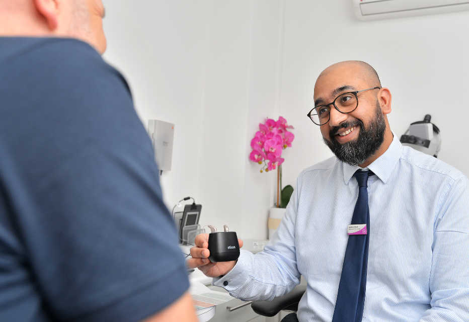Audiologist holding a hearing aid charger containing hearing aids, demonstrating its use to a patient.