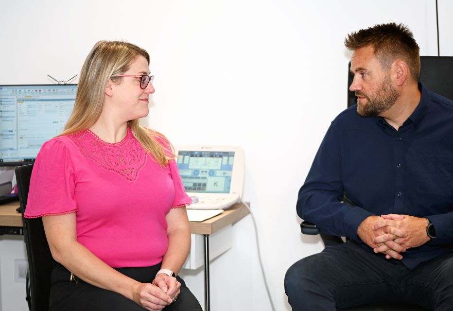 A patient and an optometrist engaged in conversation while seated in a consulting room, discussing eye care and treatment options.