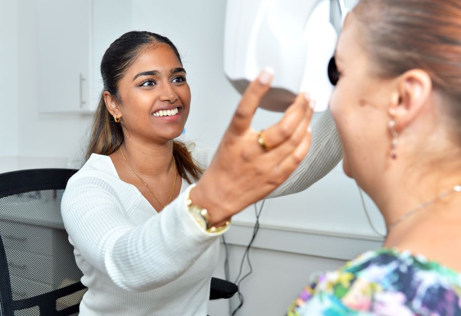 An optometrist conducting an eye examination using a phoropter, adjusting lenses while the patient looks through the device to determine their optimal prescription.