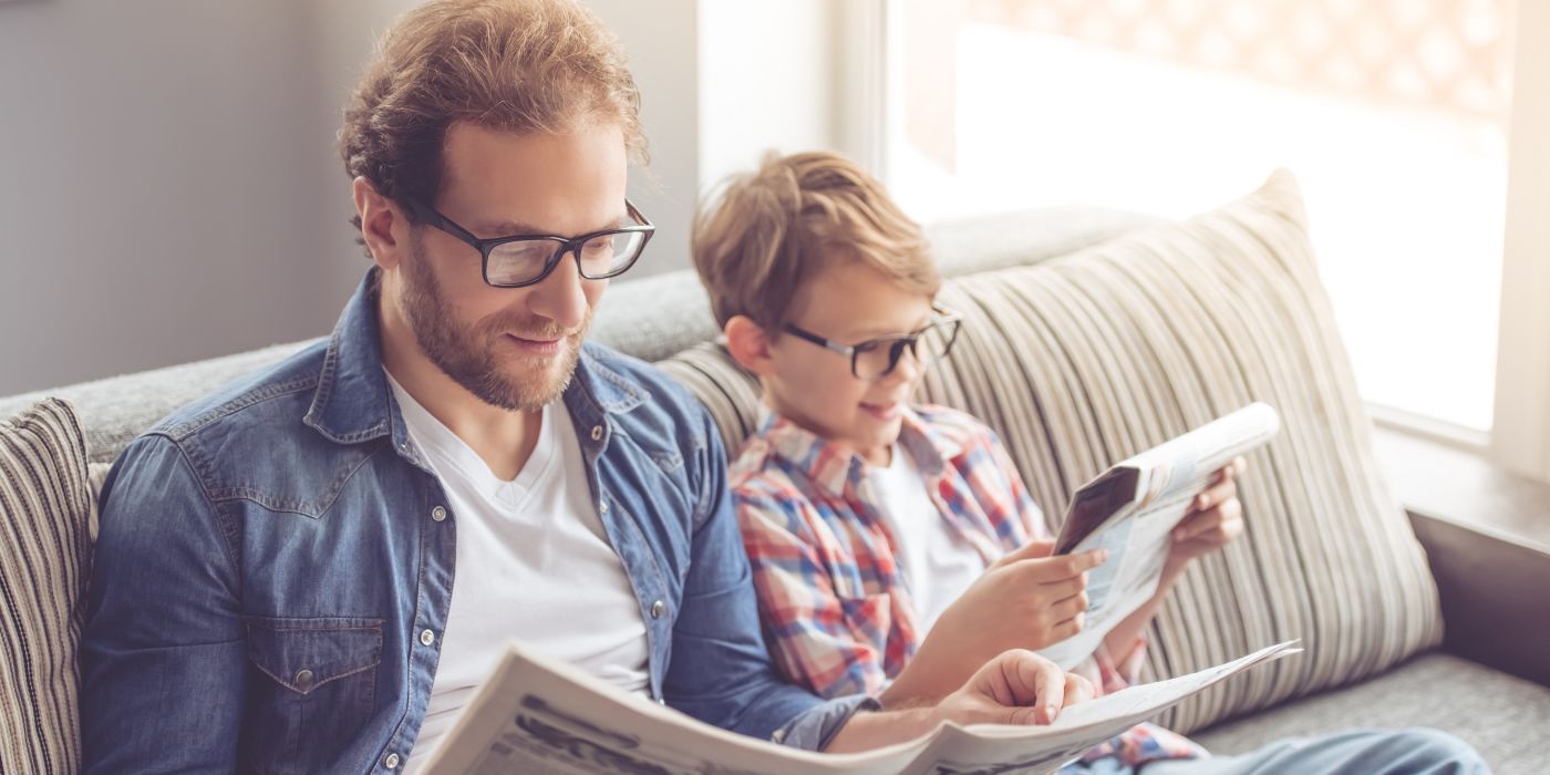 Father and son reading on sofa with glasses on