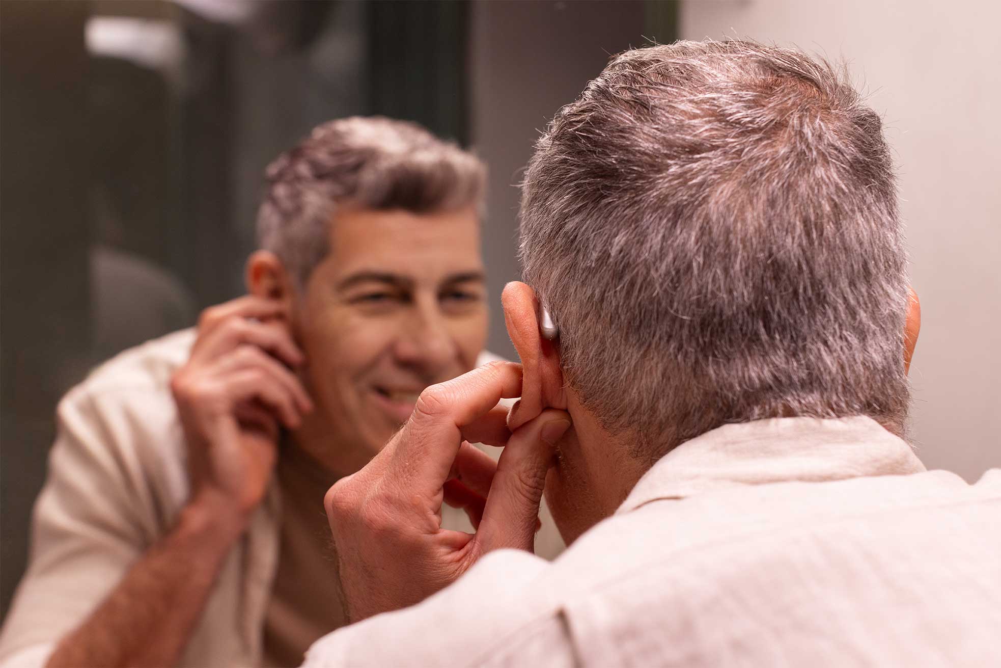 A man trying on his Phonak Audéo Sphere Infinio hearing aids in the bathroom, standing in front of the mirror to adjust them.