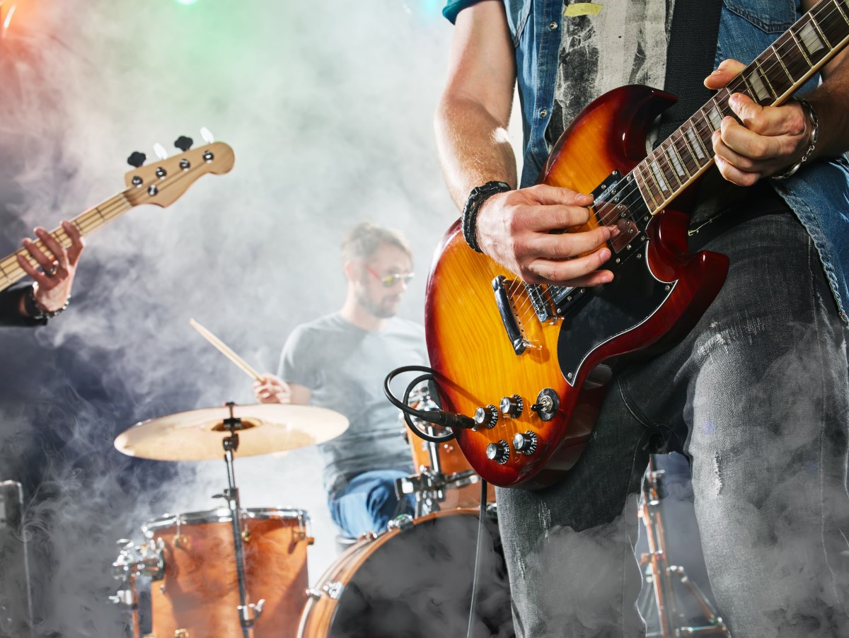 A man playing an electric guitar on stage with the rest of his group in the background.