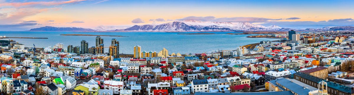 Scenic sight of Reykjavik with its colourful houses during sunset, framed by snowy mountains in the background.