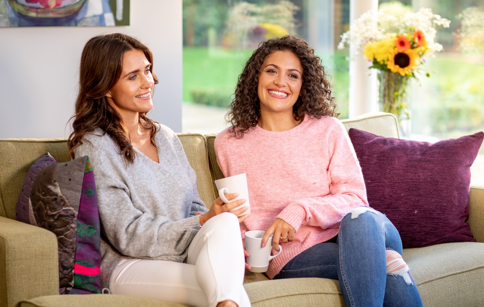 Two ladies sitting on a sofa in a sunny room, both with smiles on their faces.