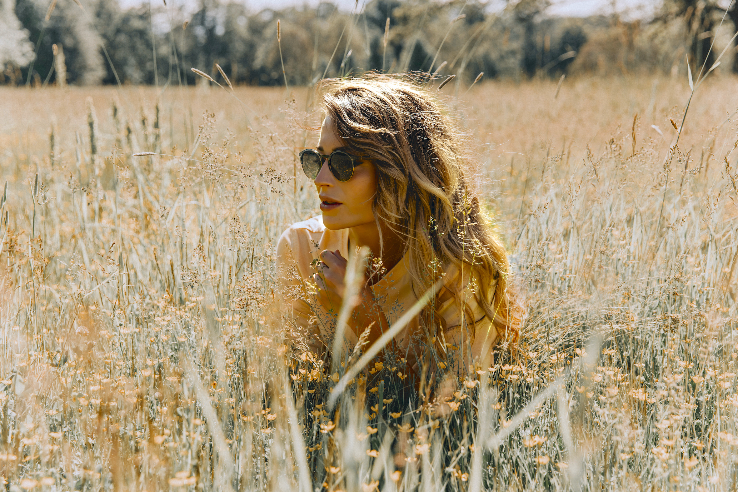 A blonde woman in a wheat field wearing sunglasses.