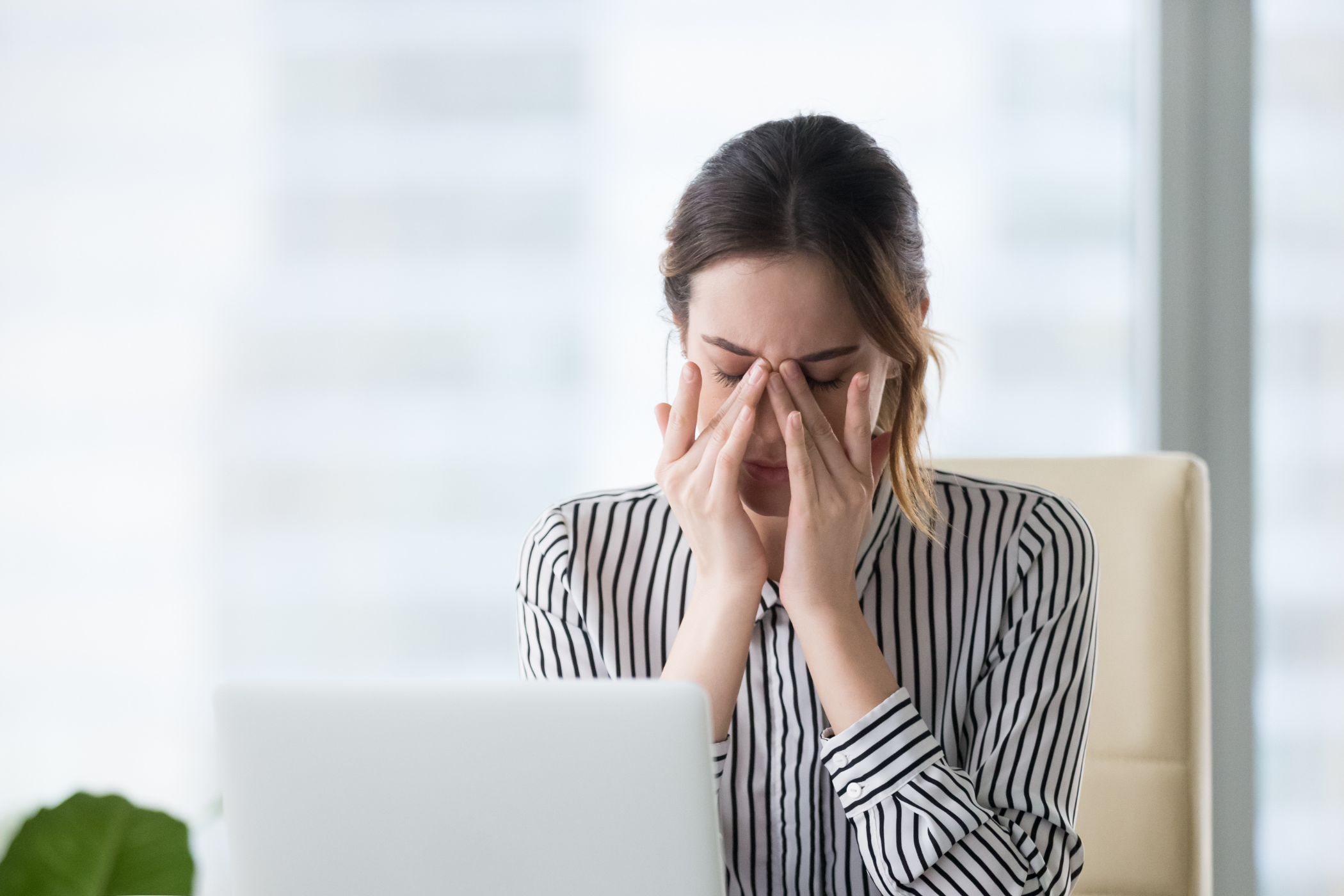 Businesswoman sitting at her desk, massaging her eyes with a pained expression.