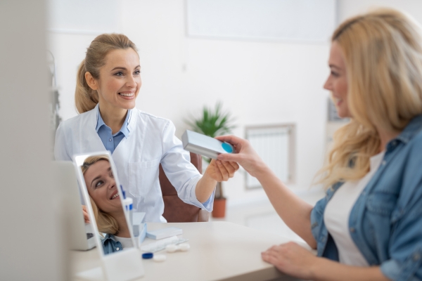 An optician handing a box of contact lenses to a patient.