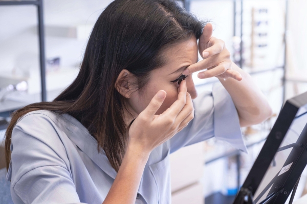 A woman inserting a contact lens into her eye while looking into a mirror.
