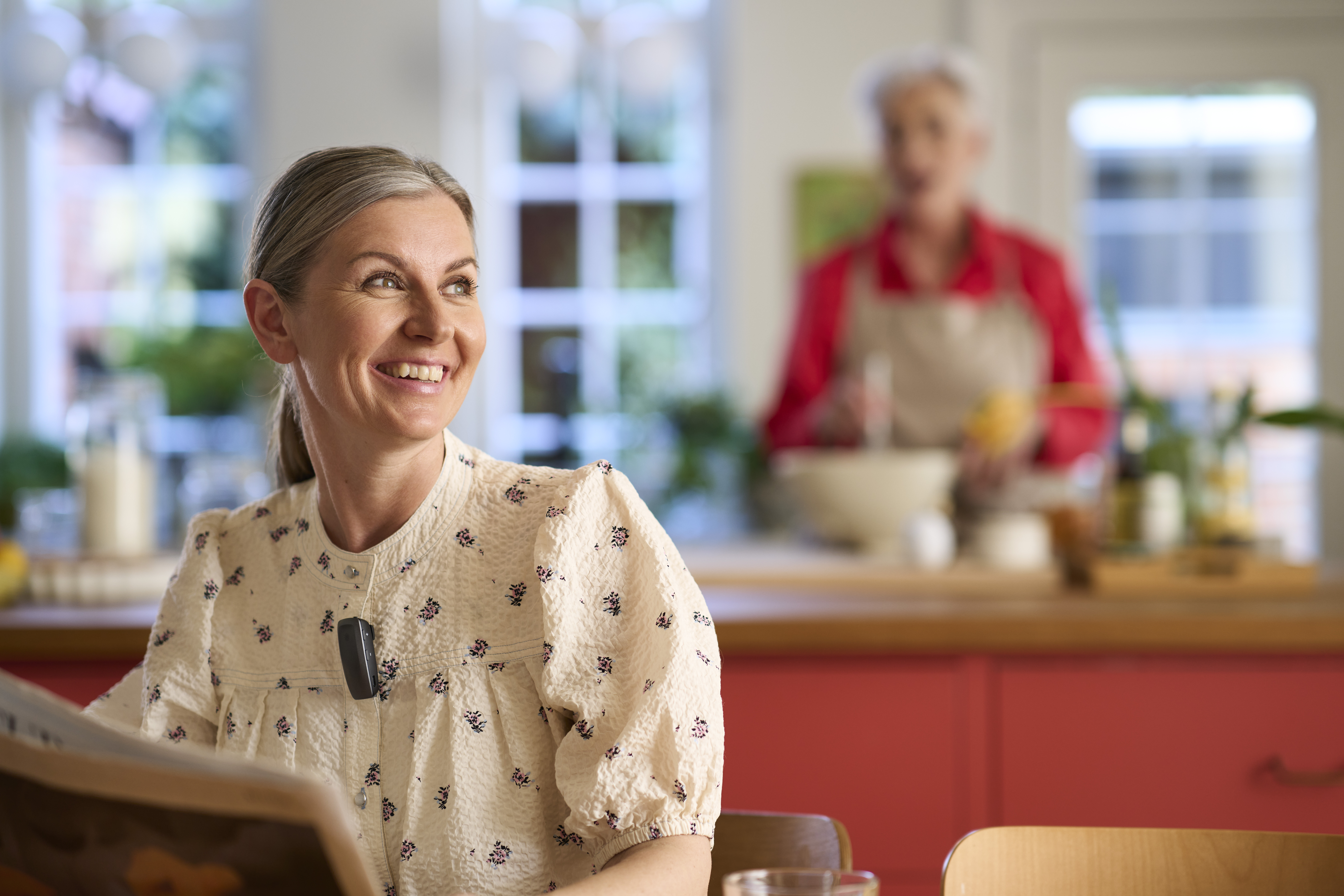 A woman wearing ReSound Nexia hearing aids in a kitchen, using the Multi-Mic accessory.
