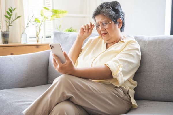 An elderly woman wearing glasses, struggling to read text on a smartphone screen by holding it close and squinting.
