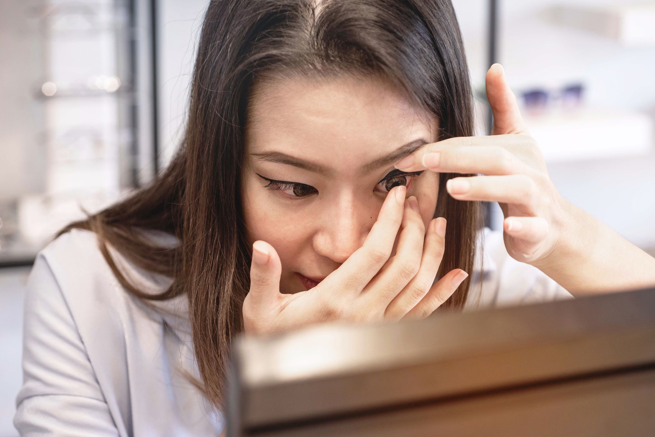 A young woman carefully inserting a contact lens into her eye.