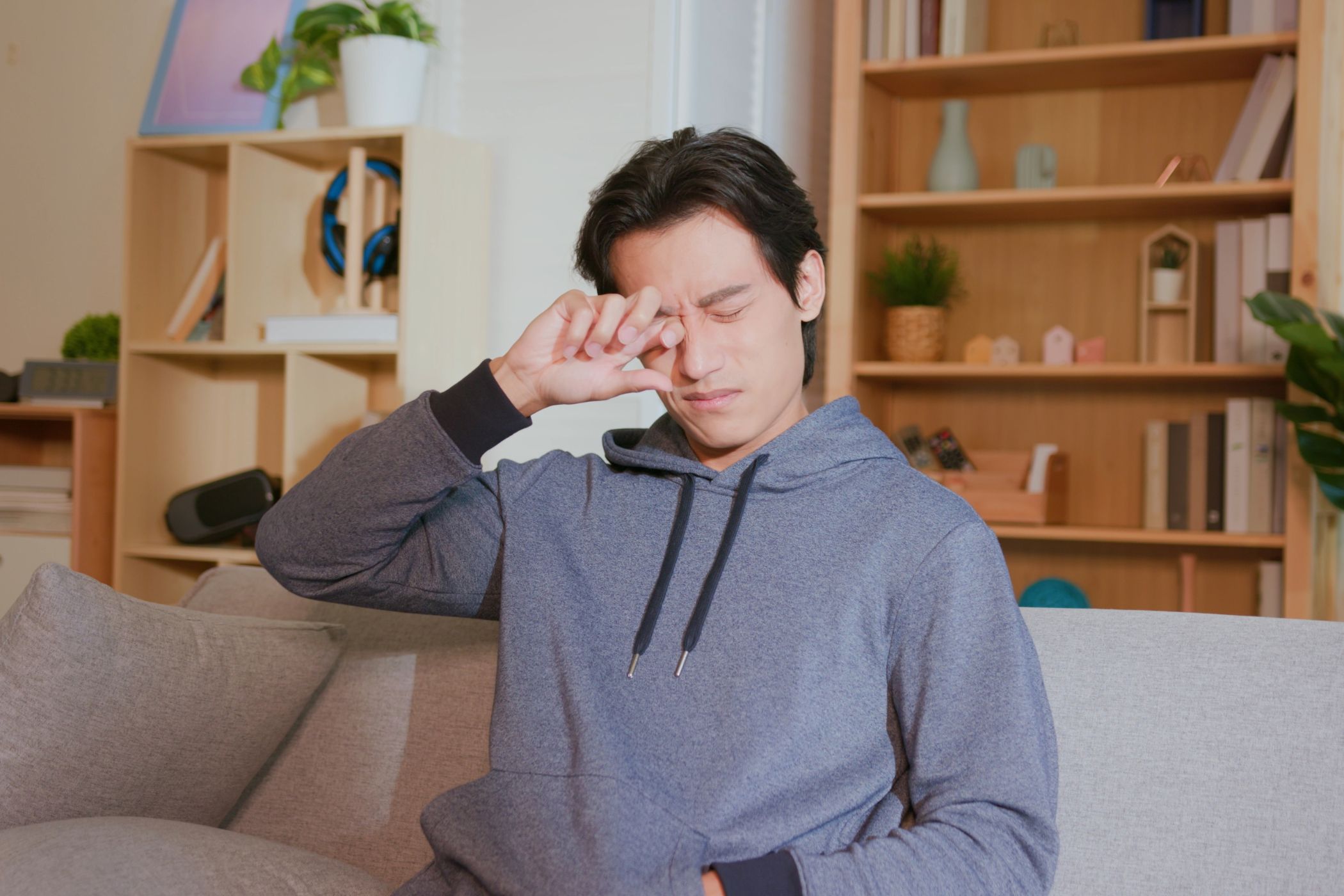 A man sitting on a sofa and rubbing his eyes.
