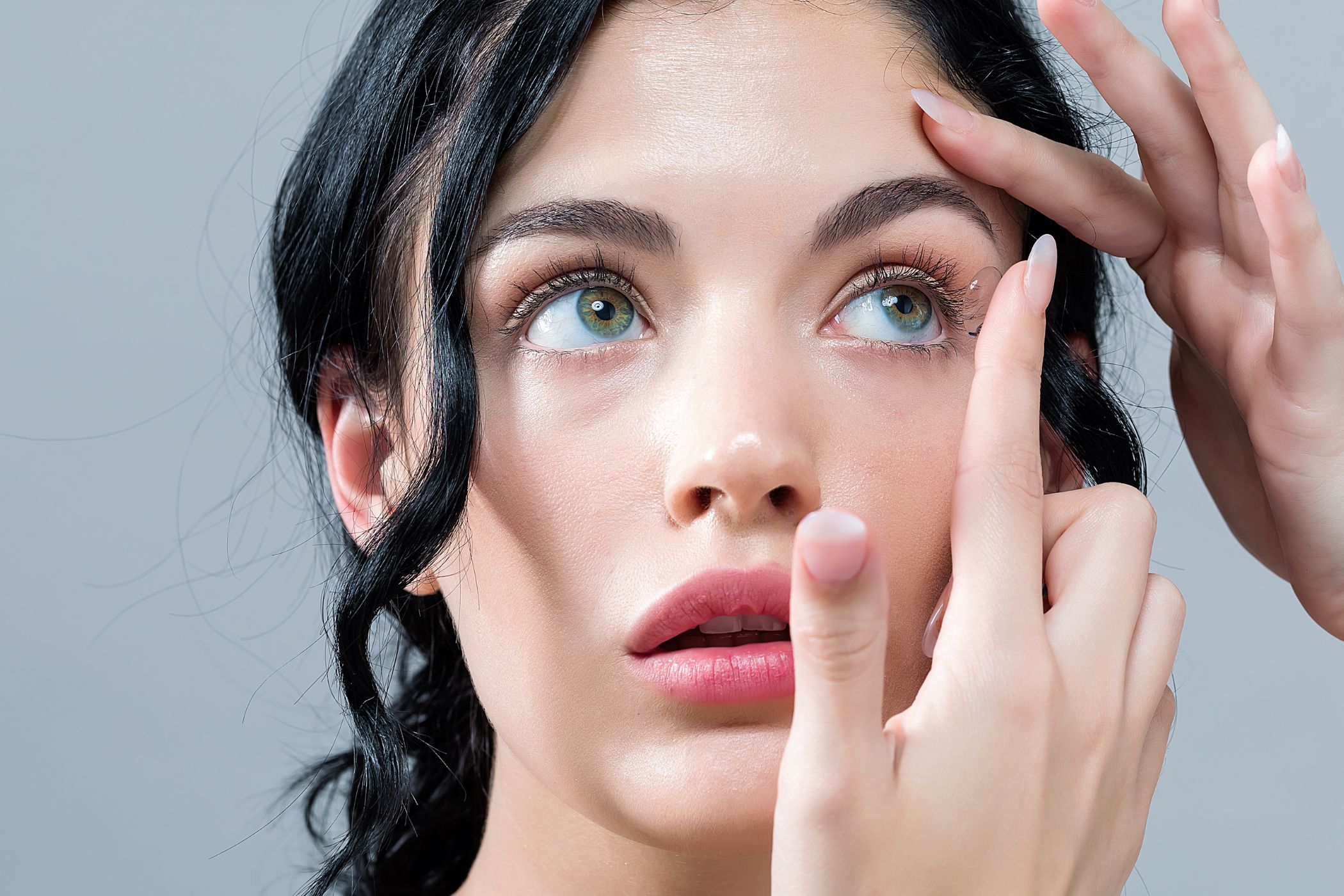 A young woman carefully inserting contact lenses into her eyes.