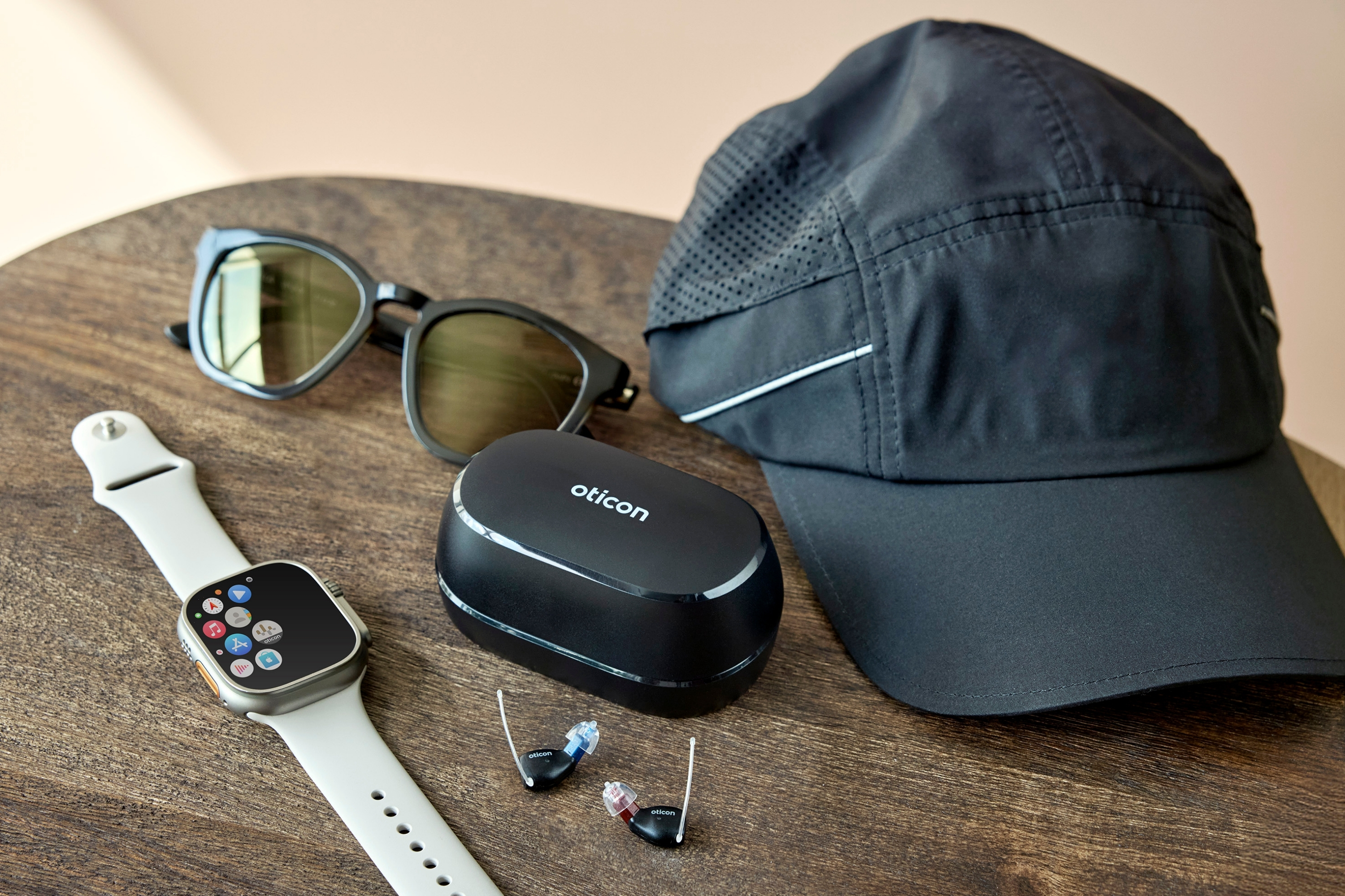 Oticon Zeal hearing aids displayed on a table alongside their case and an Apple Watch.