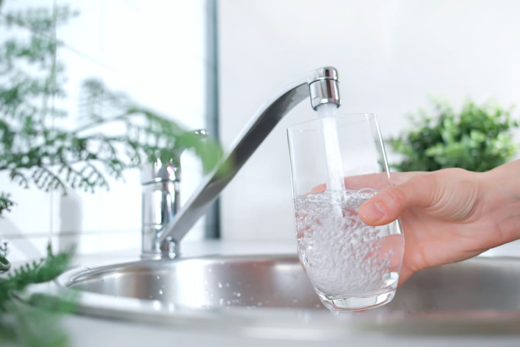 Aus dem Wasserhahn fließt sauberes Trinkwasser in ein Glas