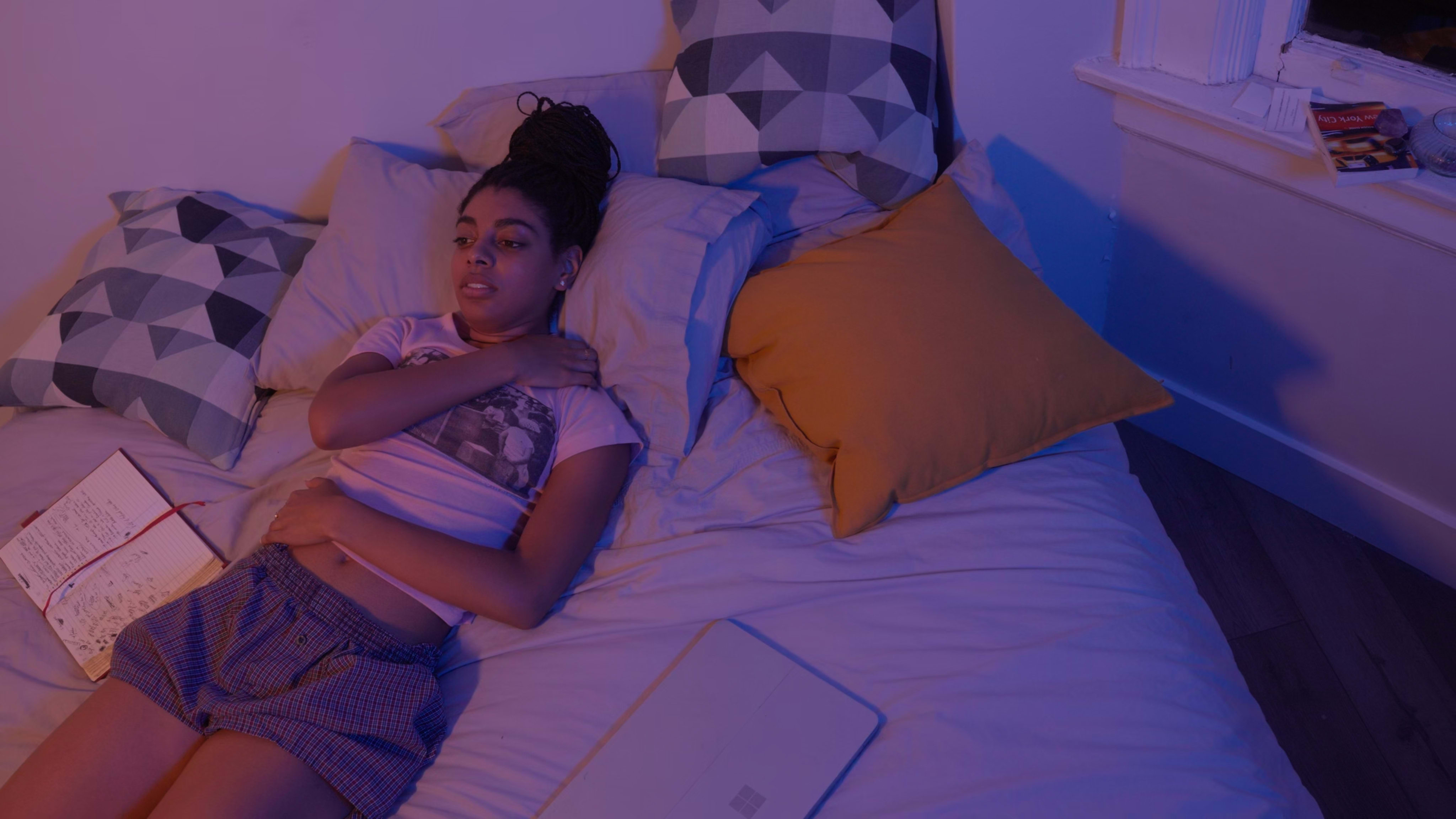 A desolate girl lying on a bed with her hands on her chest and her diary nearby.
