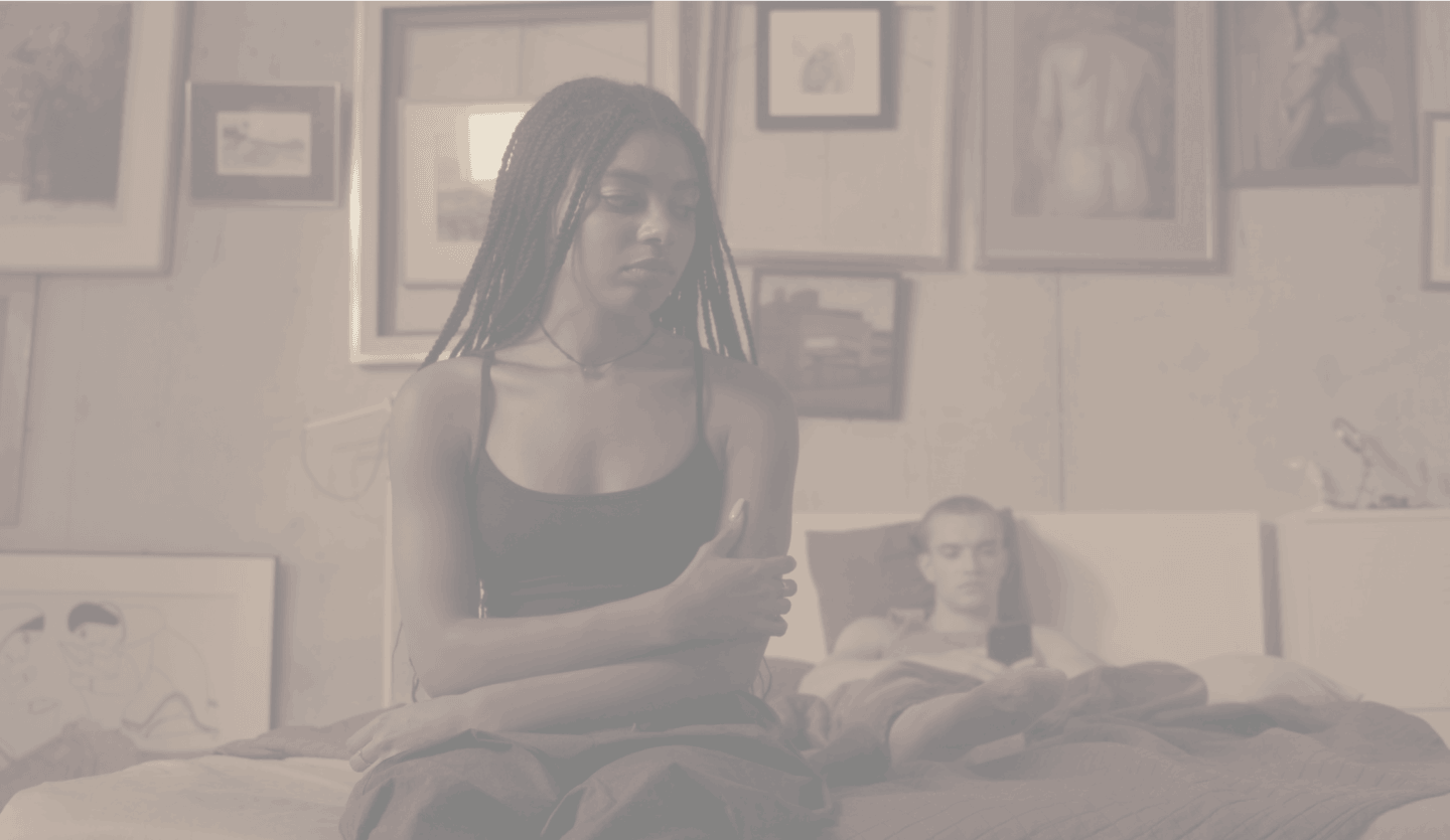 Сonfused and insecure teenage girl sitting on the edge of the bed near her boyfriend