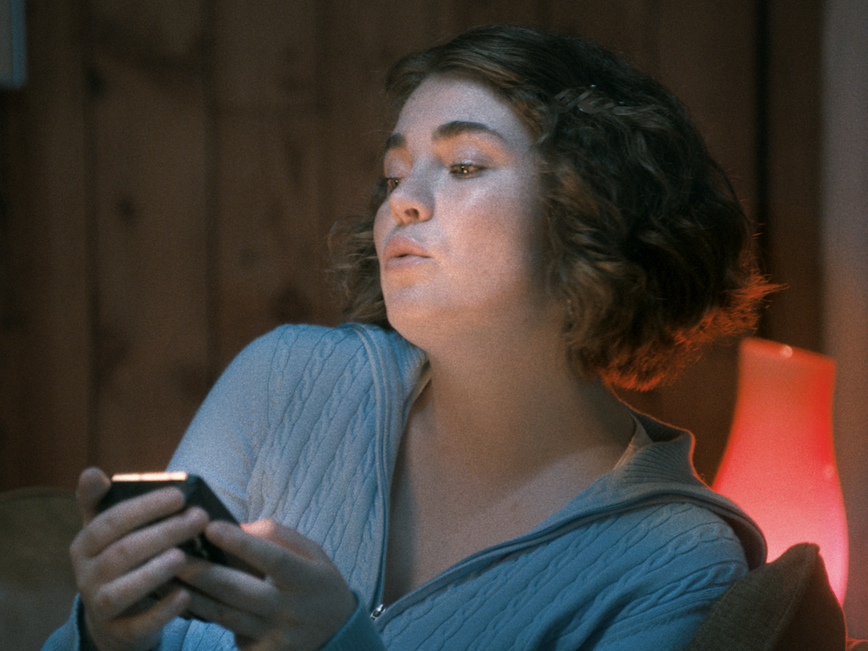 A girl mid-conversation, holding her phone in one hand and talking animatedly, possibly engaged in a chat.