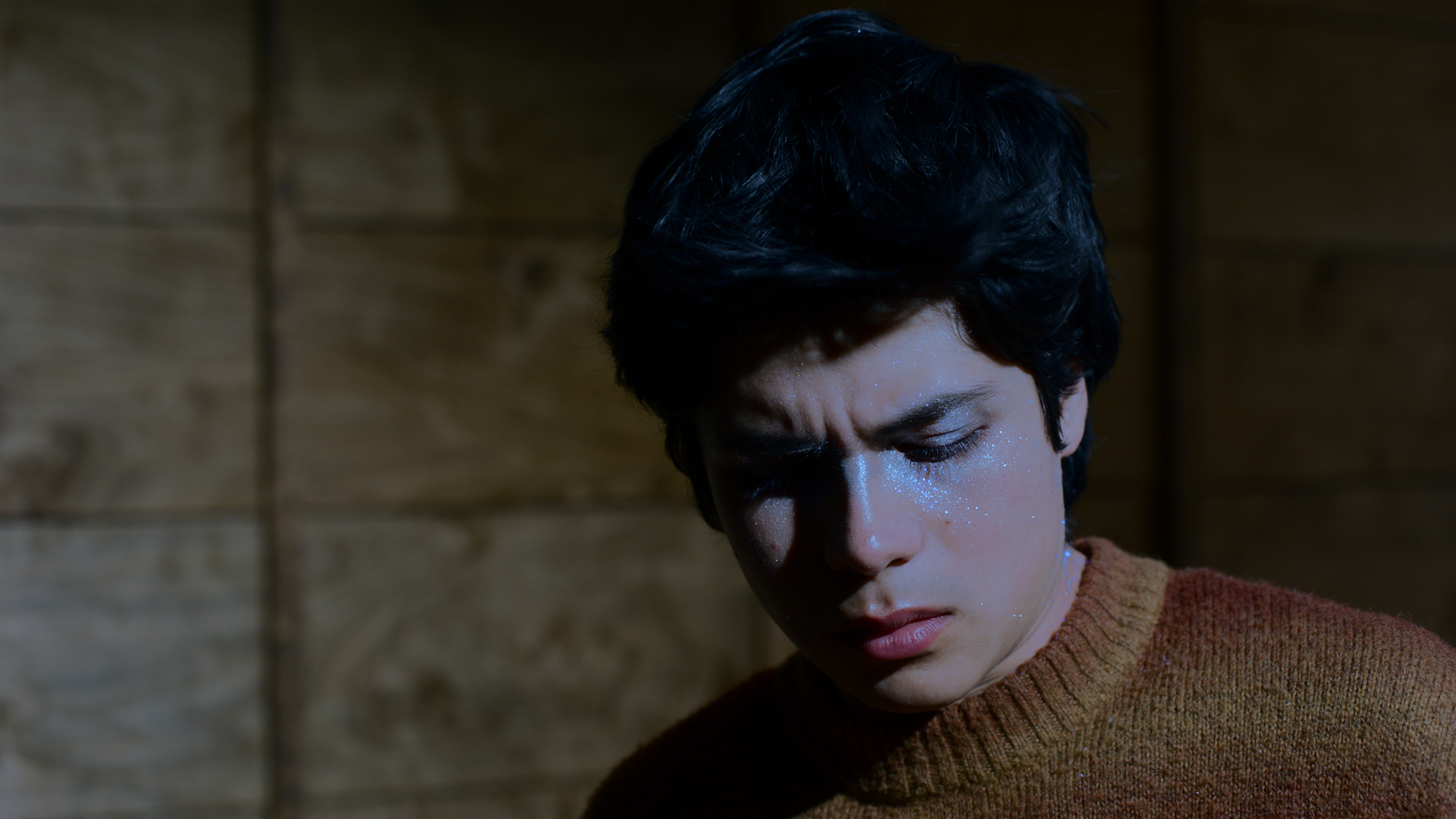 A guy frowning and looking down in a dark room.