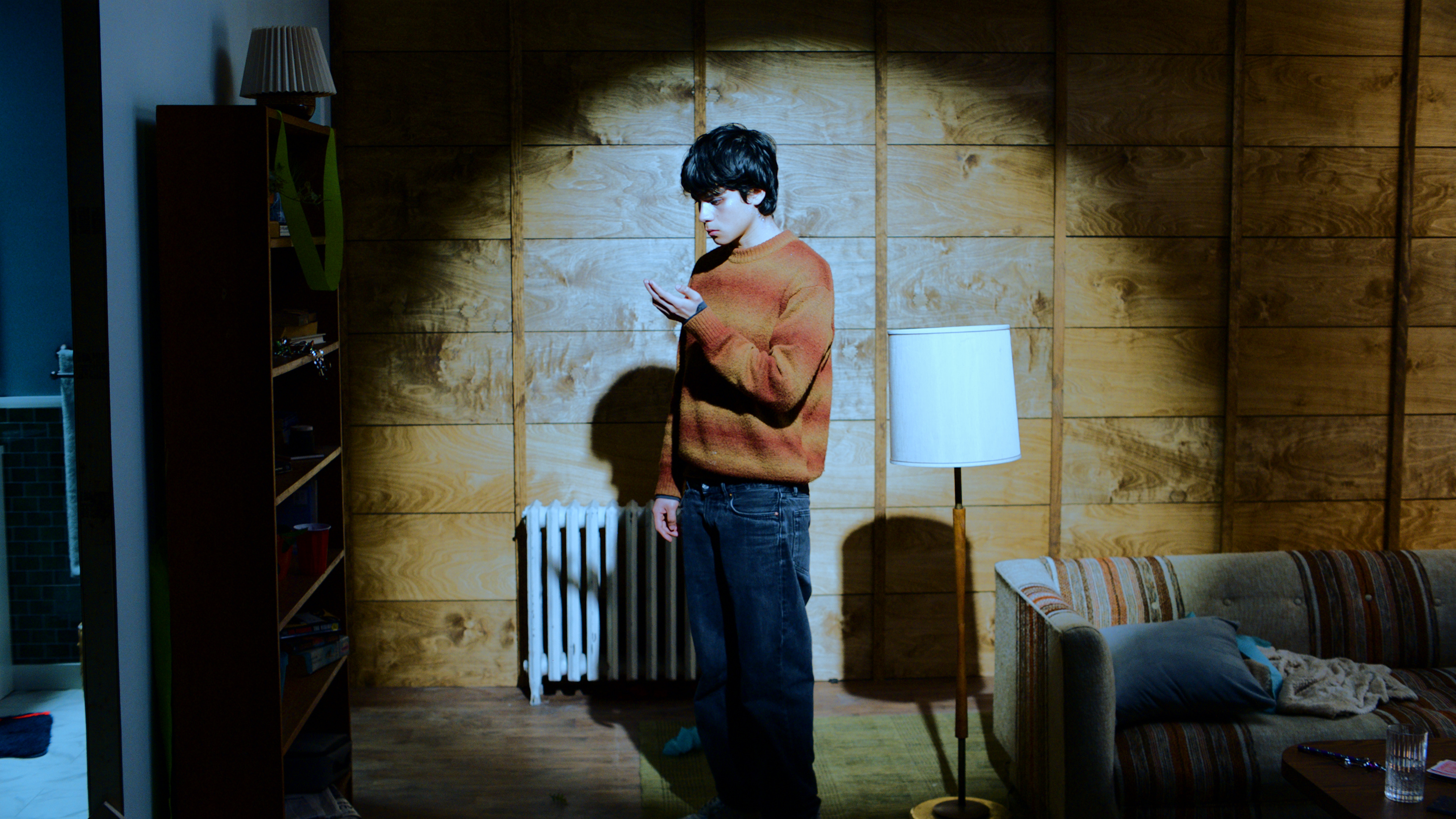 A guy standing in the middle of a room staring at his left hand.