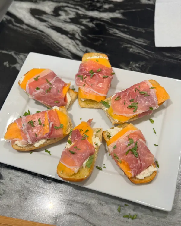 Crisp crostini topped with creamy burrata and sweet melon wrapped in prosciutto, with a hint of fresh basil