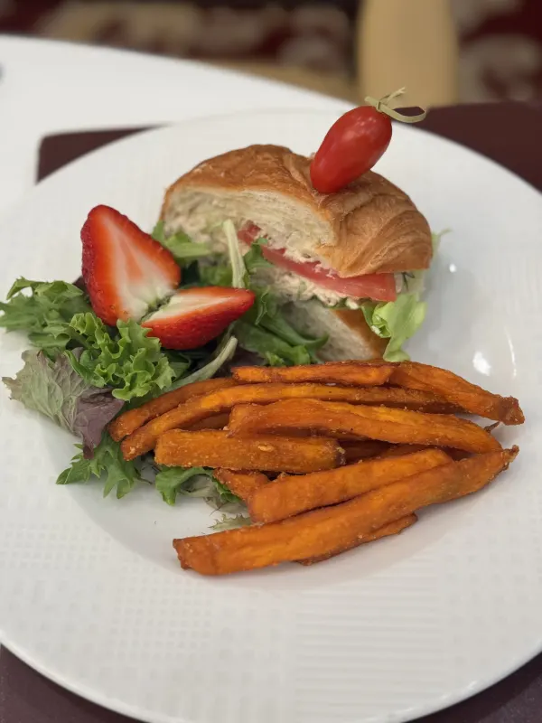 A buttery croissant layered with tuna and fresh greens, served alongside crisp sweet potato fries and a bright strawberry accent