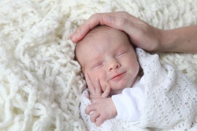 A close up of a baby with his mother's hand resting on his head.