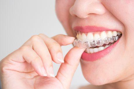 A smiling woman holding invisalign or invisible braces