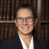 Elspeth Talbot Rice KC (a barrister with long brown hair tied back, wearing spectacles, a white shirt and black jacket). She is in front of bookshelves in the Lincoln's Inn Library