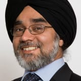 Sir Rabinder Singh smiling, wearing a black turban, glasses and with a balck beard flecked with gray