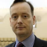 Rev Alexander MacGregor softly smiling wearing a suit and tie.