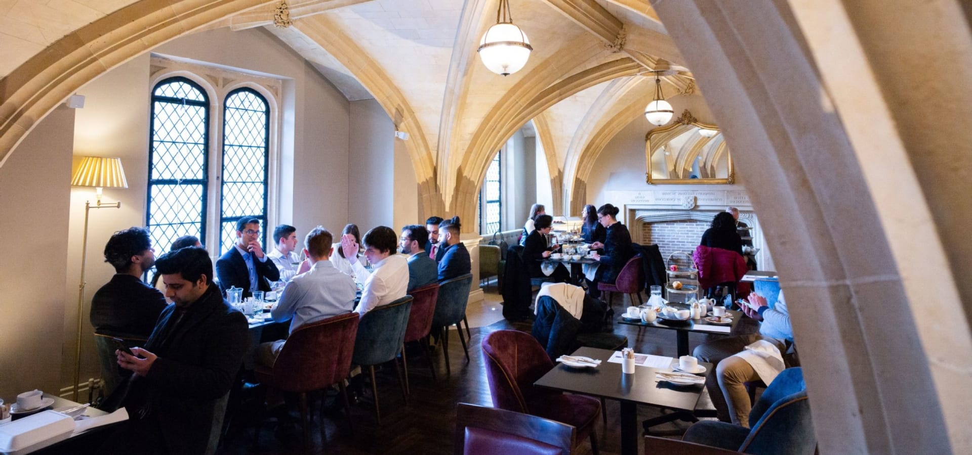 People dining in an elegant restaurant with arched ceilings and soft lighting. The atmosphere is lively yet intimate, with groups engaged in conversation.