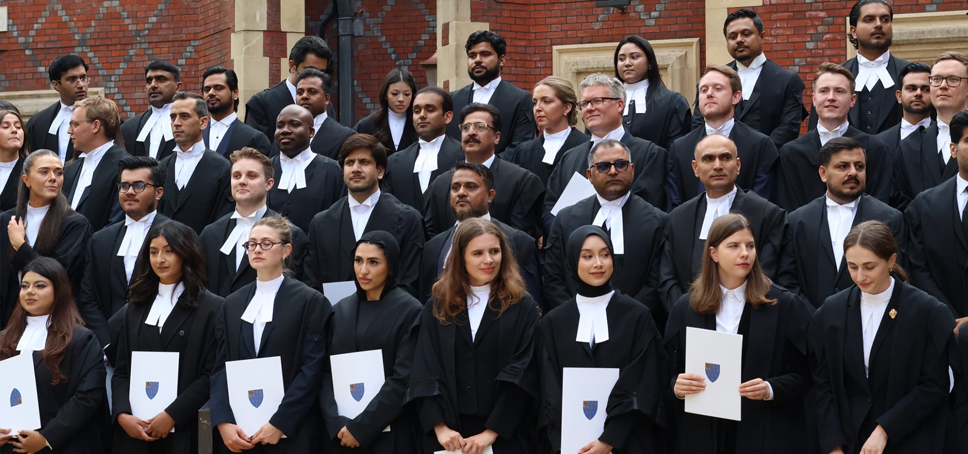 Group photograph of newly qualified barristers following a Call to the Bar ceremony at Lincoln's Inn, holding certificates outside on the steps in front of the Great Hall building