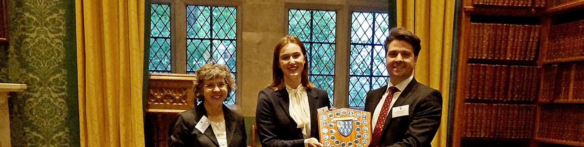 Judge Janet Bignell KC with winners Eve Handley and James Forrester. The winners are holding a trophy.