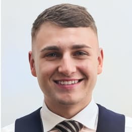 Ryan Zwetschnikow in a wasitcoat and tie, smiles for the camera. He has short cropped hair.