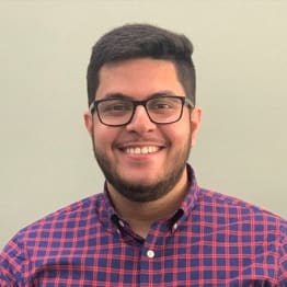 Saurabh Bhalla in a red and blue checked shirt. He is smiling, wars dark thick framed glasses and has a very short beard/stubble