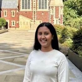 Tisha Shinde in a white jumper, smiling, standing in front of the treasury building at Lincoln's Inn.
